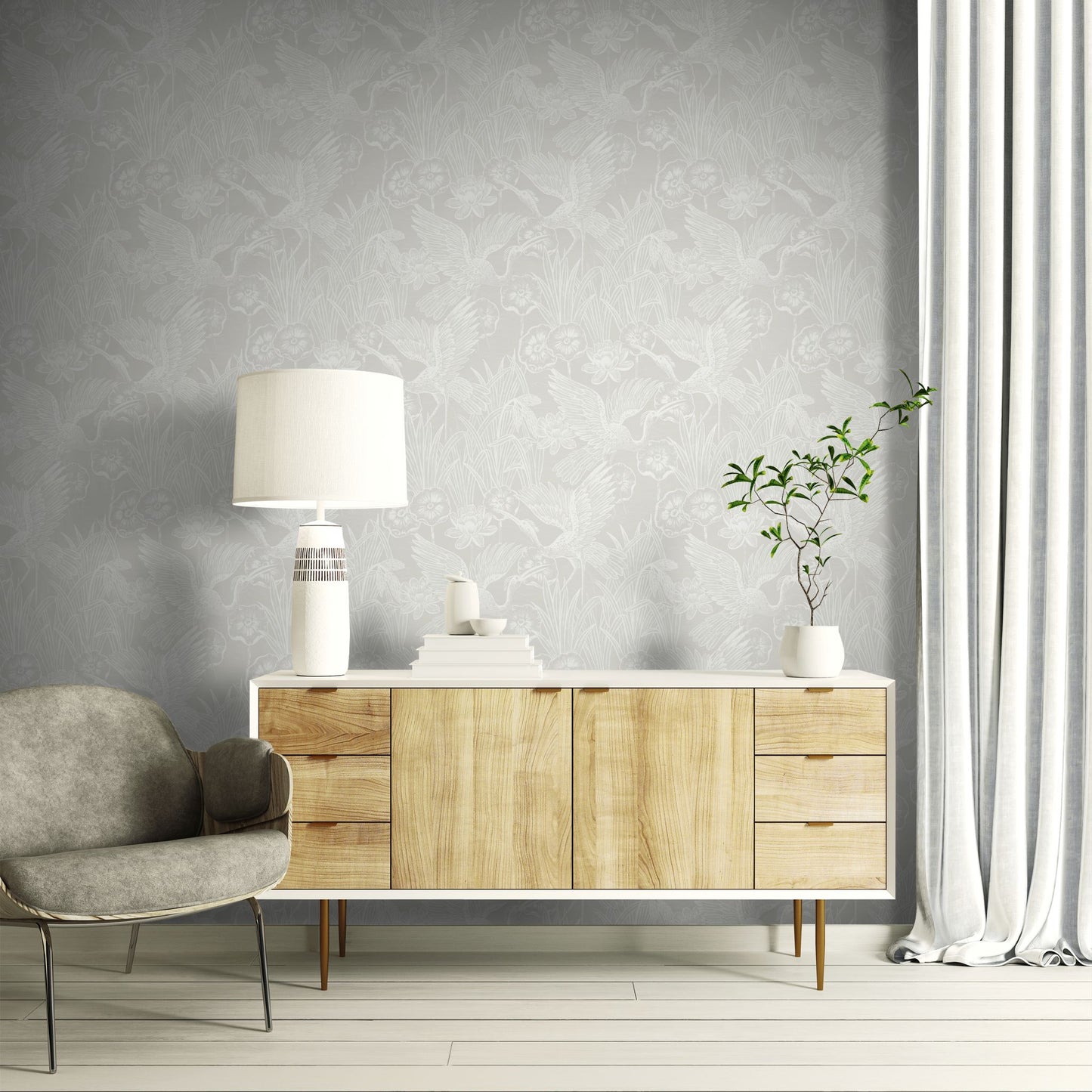 Wooden sideboard with a lamp and plant against a wall decorated with White/Off White Marsh Heron Wallpaper.
