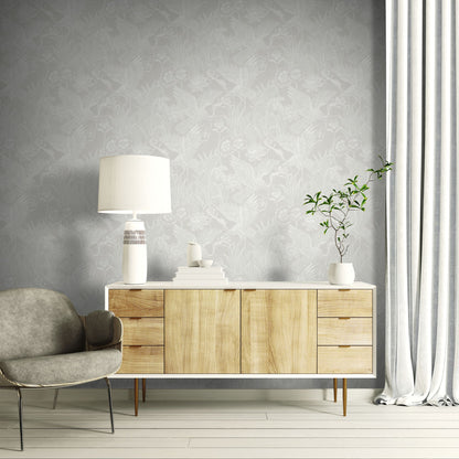 Wooden sideboard with a lamp and plant against a wall decorated with White/Off White Marsh Heron Wallpaper.
