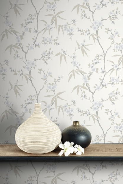 Two vases on a wooden surface with wall decorated with White/Off White Blossom Spring Flower Wallpaper.
