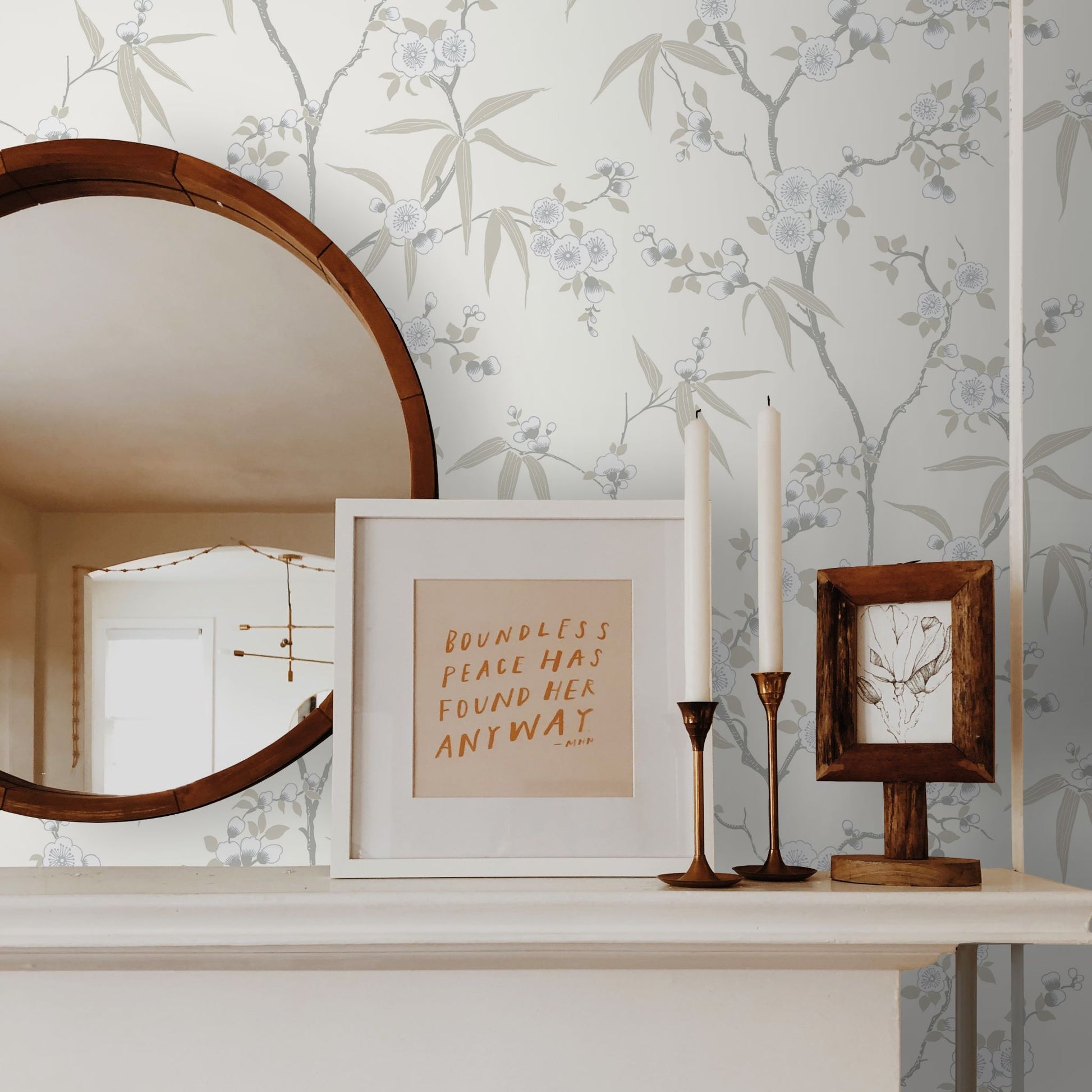 Decorative shelf with framed quote, candles, and mirror against a wall decorated with White/Off White Blossom Spring Flower Wallpaper.
