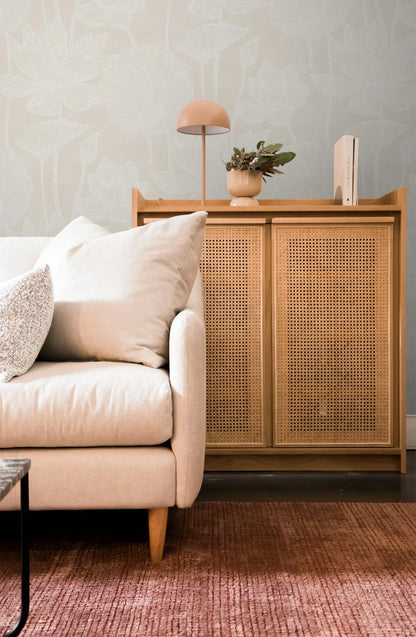 Light sofa beside a wooden cabinet with lamp and plant, on a pink rug with Lily Flower Wallpaper in the background.
