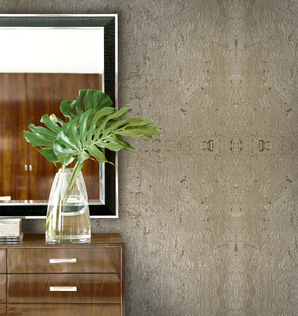 Large green monstera leaf in a glass vase on a dresser, beside a mirror with Algarve Cork Grasscloth Naturals wallpaper.