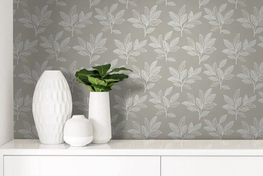 Three white vases, one with a green plant, sit on a white surface against Stylized Leaves Peel Stick wallpaper.