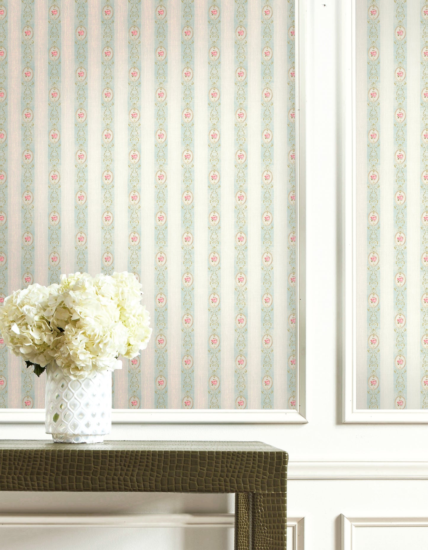 White hydrangeas in a patterned vase sit before Flower Stripe Wallpaper and white paneling.