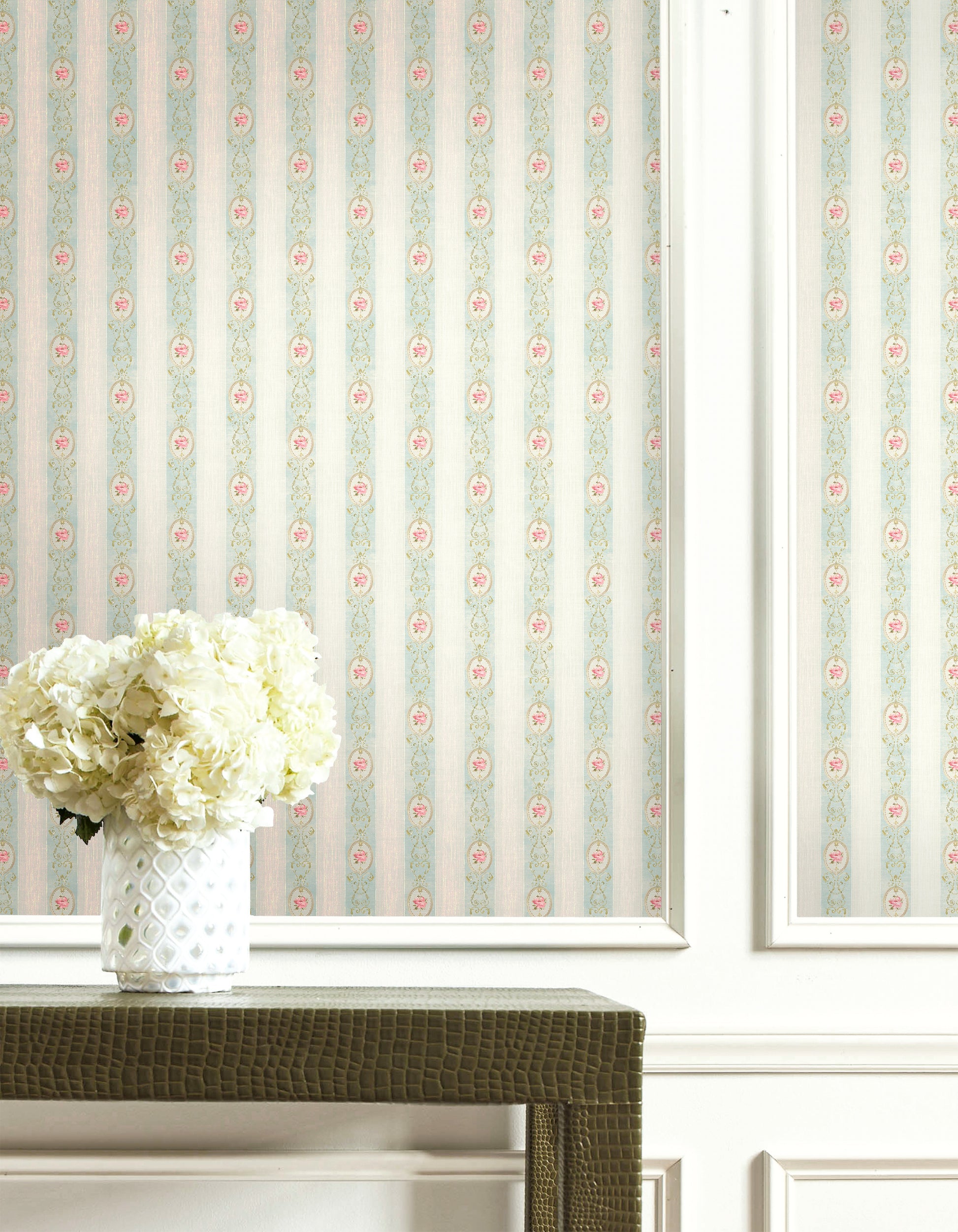 White hydrangeas in a patterned vase sit before Flower Stripe Wallpaper and white paneling.