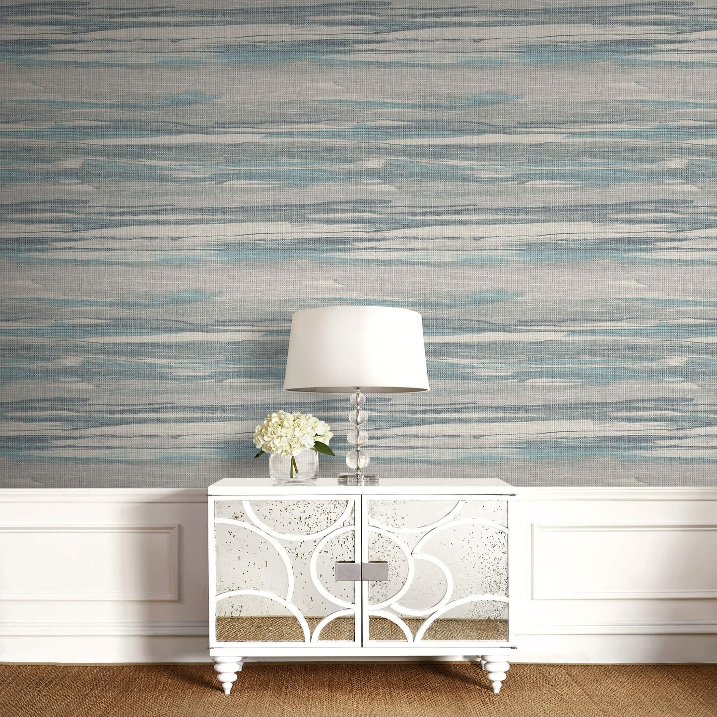 White sideboard with decorative lamp and flowers against a patterned Gray & Green Grasscloth Waves Wallpaper.
