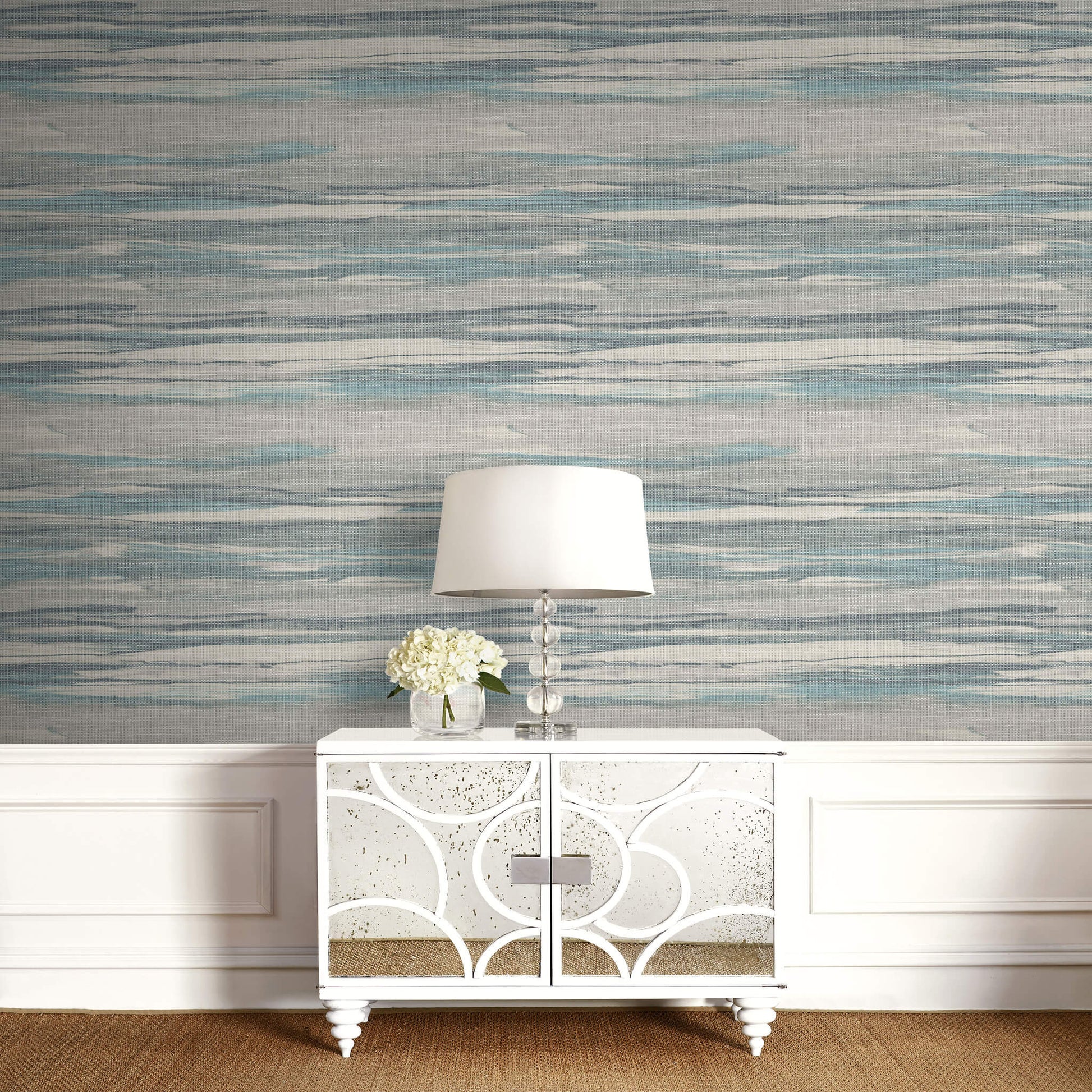 White sideboard with decorative lamp and flowers against a patterned Gray & Green Grasscloth Waves Wallpaper.
